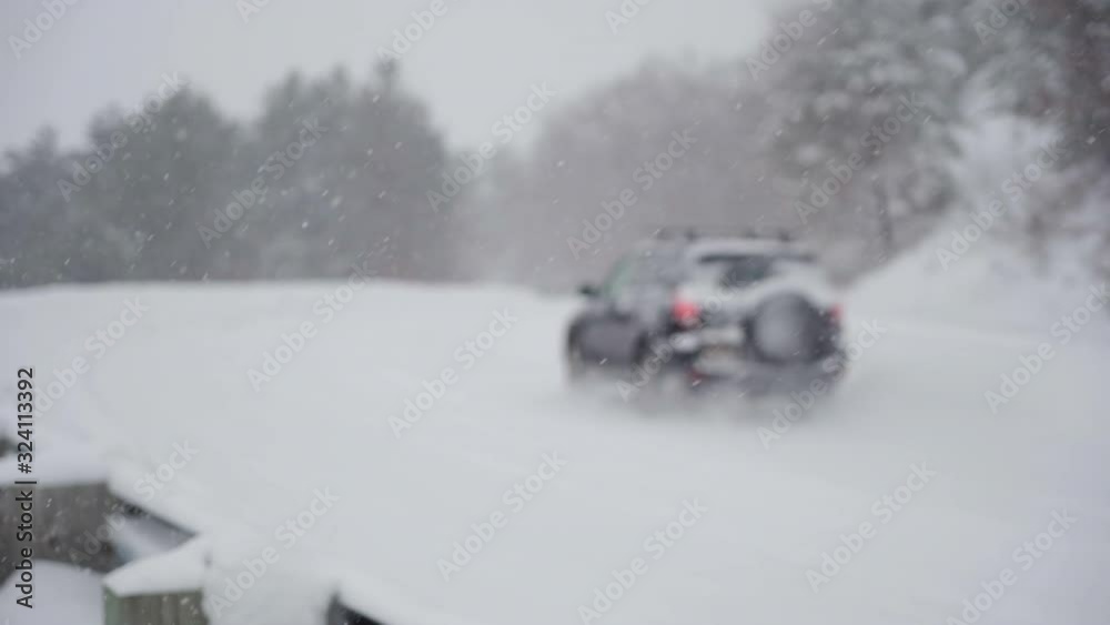 A defocused small SUV drives through a snow storm on a back road in slow motion. A defocused small SUV drives through a snow storm on a back road in slow motion.