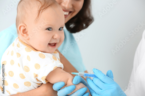 Pediatrician vaccinating little baby on light background photo