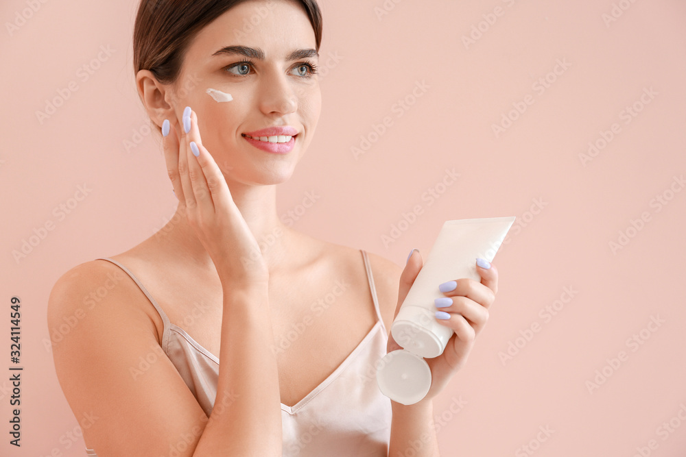 Beautiful young woman applying cream on her face against color background Beautiful young woman applying cream on her face against color background