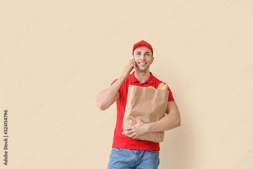 Handsome worker of food delivery service talking by phone on color background