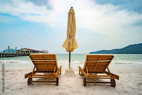 Beach calm scene with sunbeds and straw umbrellas under coconut palms close sea. Tropical paradise with chaise lounges on white sand, beautiful travel card background photo