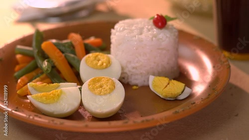 Boiled egg being broken with fork and knife on marom dish with rice and vegetables photo