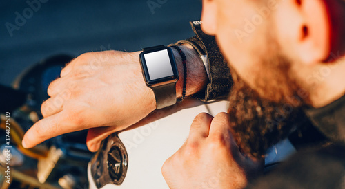 Upper view of a bearded caucasian biker looking at his watches with blank space before going on a trip by motorcycle photo