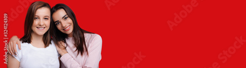 Two lovely caucasian girls embracing and smiling are posing on red background with blank space