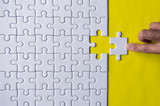 Hand putting jigsaw puzzle white color on yellow background