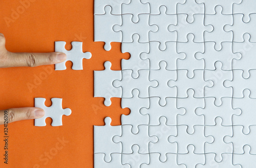 Hand putting jigsaw puzzle white color on orange background