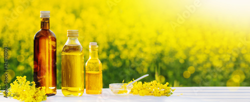 rapeseed oil in bottles on white wooden table on background flowering rape field photo