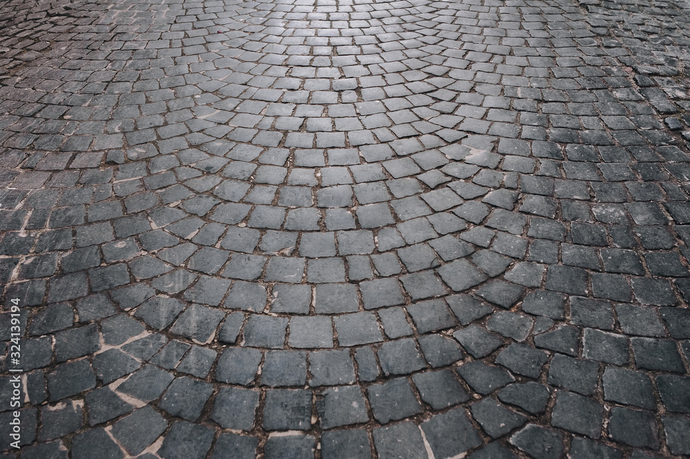 The gray paving stones laid out in a semicircle. The texture of the old dark stone. Road surface. Vintage, grunge.