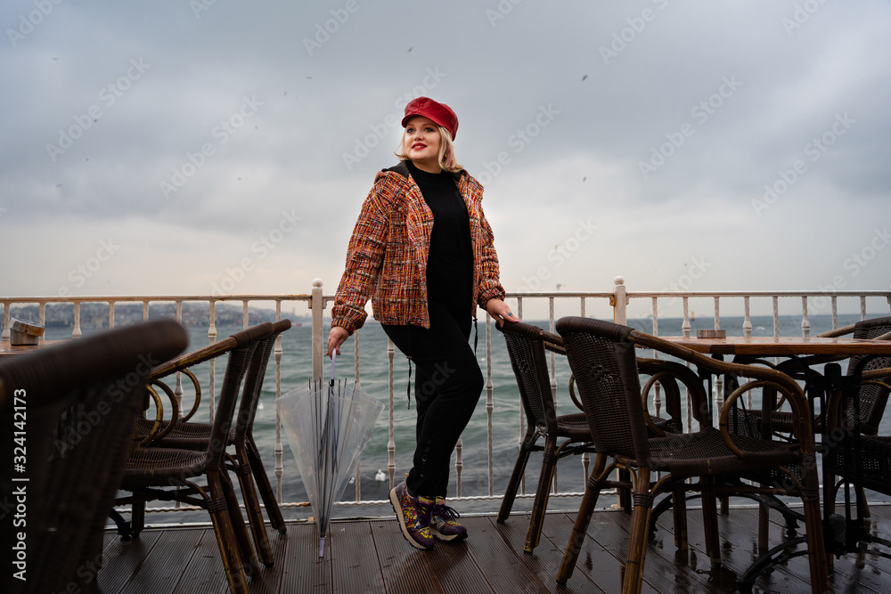 a girl with an umbrella and a red cap stands in the rain by the sea