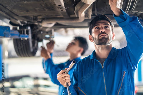 Canvas Print Vehicle service maintenance handsome mens checking under car condition on lifter in garage