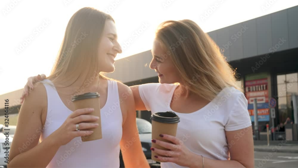 4k video of two smiling and laughing female friends having good time and drinking coffee while walking on street at sunset 4k video of two smiling and laughing female friends having good time and drinking coffee while walking on street at sunset