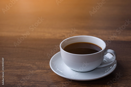 A white cup of coffee on wooden table with sunlight. Space for text. Relax in the morning. Relaxation concept