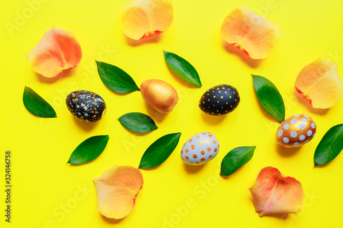 Fototapeta Naklejka Na Ścianę i Meble -  Festive easter background. Golden, black and white stylish pinted eggs with leaves and rose petals on yellow background.