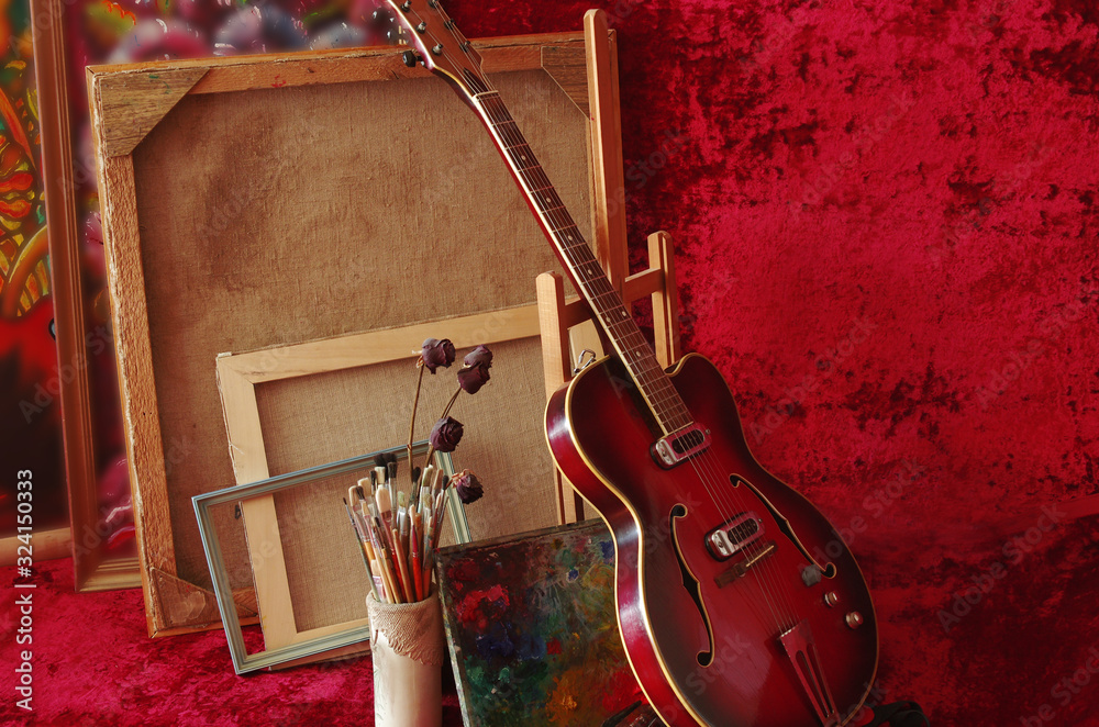 Φωτογραφία Jazz electric guitar, canvases, frames, art palette and brushes on the background of burgundy drapery