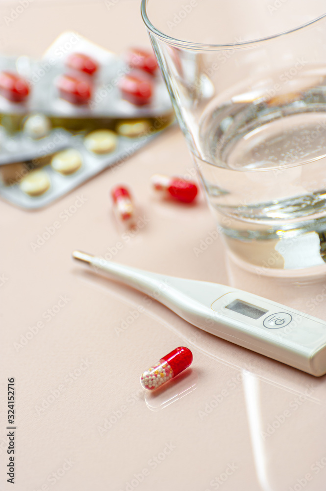 Antibiotic tablet, a glass of water and a thermometer on a beige pastel background. Antibiotic tablet, a glass of water and a thermometer on a beige pastel background.