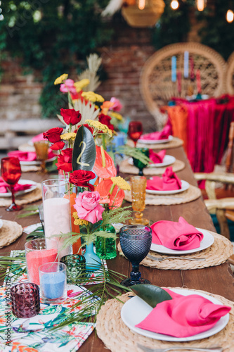 Banquet tables decorated in tropical style decor  dishes on the tables with pink napkins  glasses  candles  colorful flowers