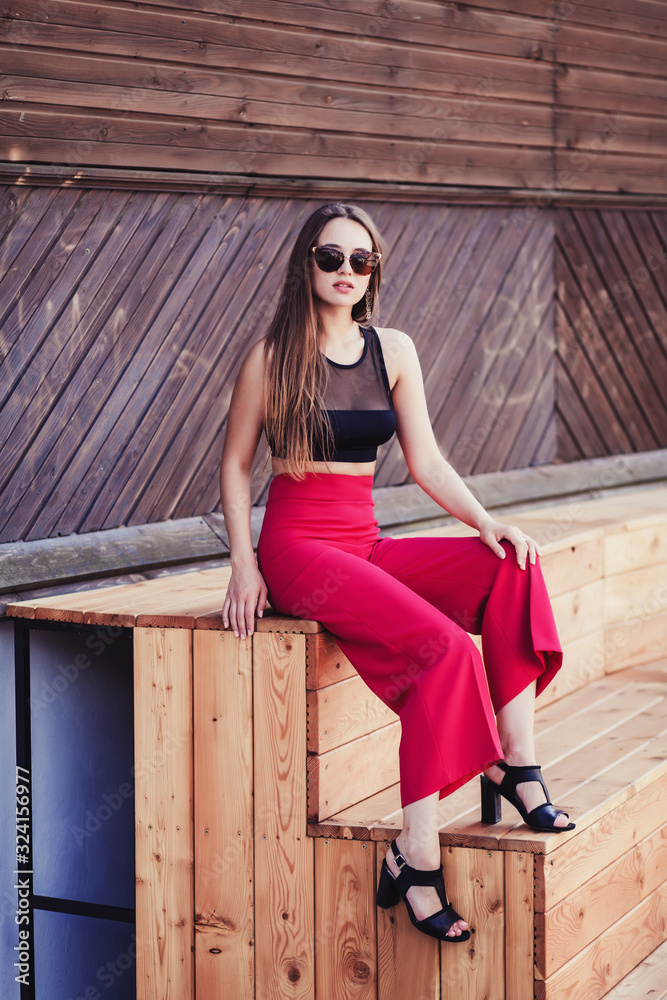 charming lady in red trousers and a black top poses in a street space charming lady in red trousers and a black top poses in a street space