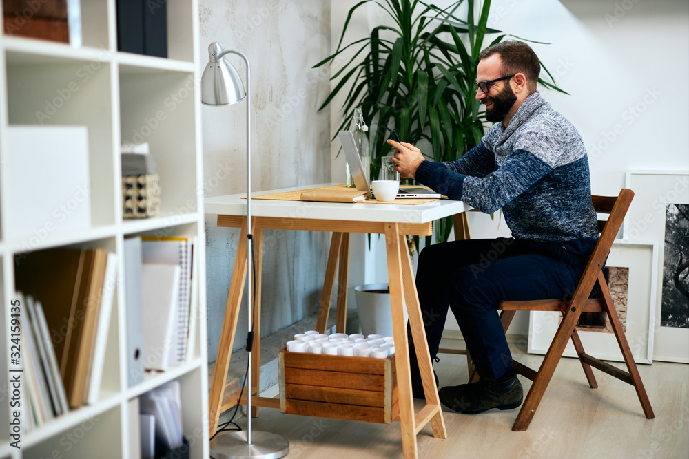 Attractive freelance male sitting in modern office and typing on sell phone.