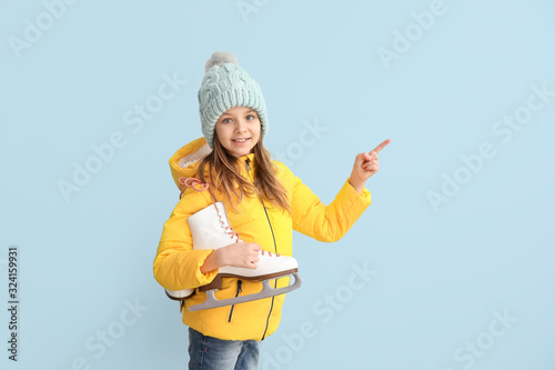 Cute little girl with ice skates showing something on color background