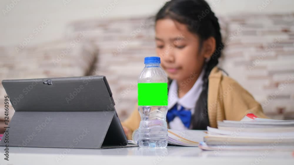 Little Asian girl doing homework with happiness, green screen and select focus on drinking bottle, shllow depth of field, Thai girl in student kindergarten uniform Little Asian girl doing homework with happiness, green screen and select focus on drinking bottle, shllow depth of field, Thai girl in student kindergarten uniform