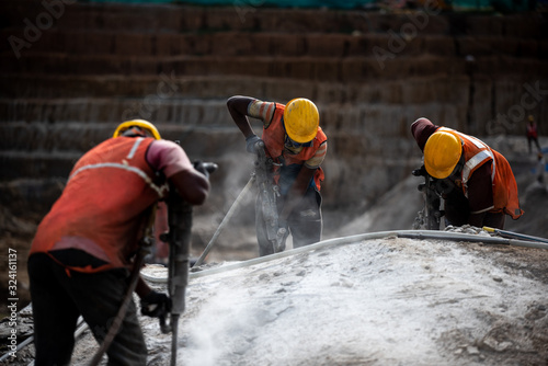 Construction labour workers dig through a rock using electronic digging machines photo