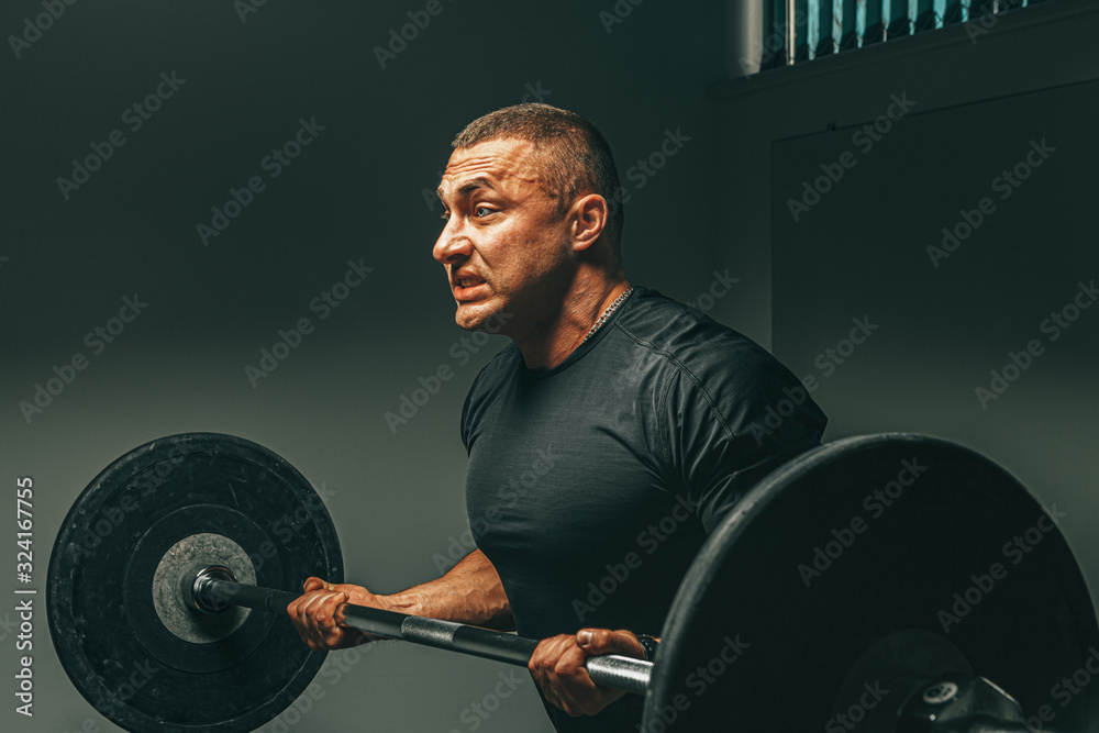 Muscular man in black sportswear lifting barbell in a gym