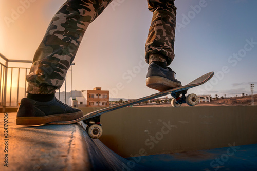 Primer plano de las piernas de un joven patinador a punto de saltar una rampa al atardecer photo