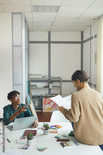 Two young designer sitting at the table and discussing sketches of their new project in workshop