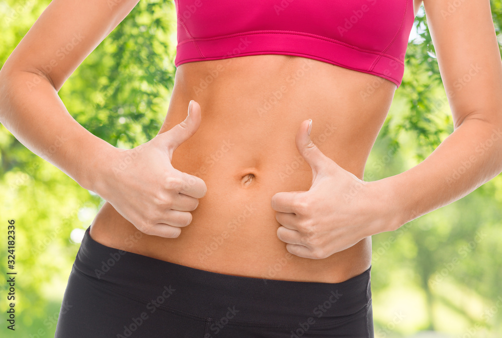 fitness, diet and people concept - close up of female abdomen and hands showing thumbs up over green natural background fitness, diet and people concept - close up of female abdomen and hands showing thumbs up over green natural background