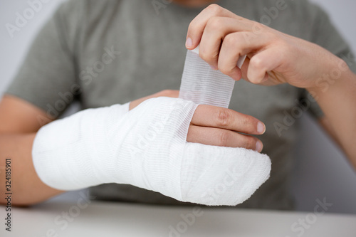 fracture and first aid concept - close up of man bandaging himself