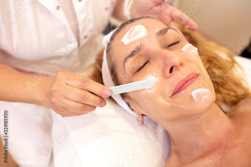 Cosmetician putting face cream on her client   s skin