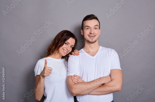 Beautiful young couple on a gray background shows finger like sign.