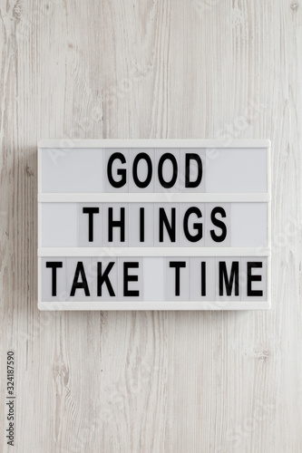 'Good things take time' words on a lightbox on a white wooden surface, top view. Overhead, from above, flat lay.