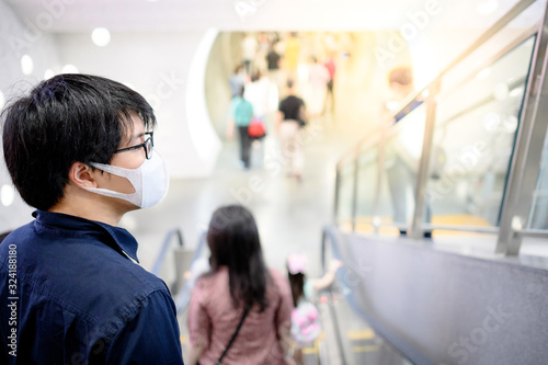 Asian man wearing surgical face mask in subway station with crowded people walking pass. Wuhan coronavirus (COVID-19) outbreak prevention in public area. Health care and medical concept