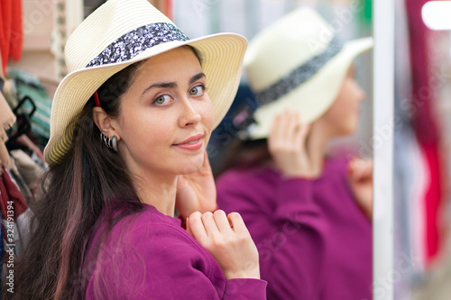A young Caucasian woman tries on a straw hat for a vacation. Fitting room in the background. Close up. The concept of buying clothes