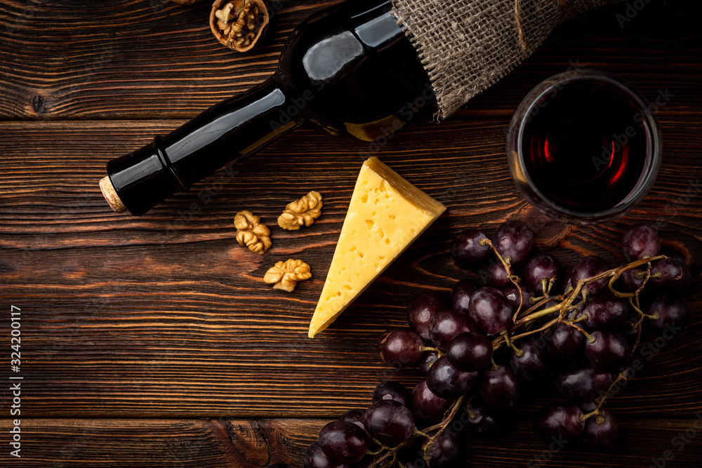 Obraz premium Red wine, grape, cheese and walnut on dark wooden background.