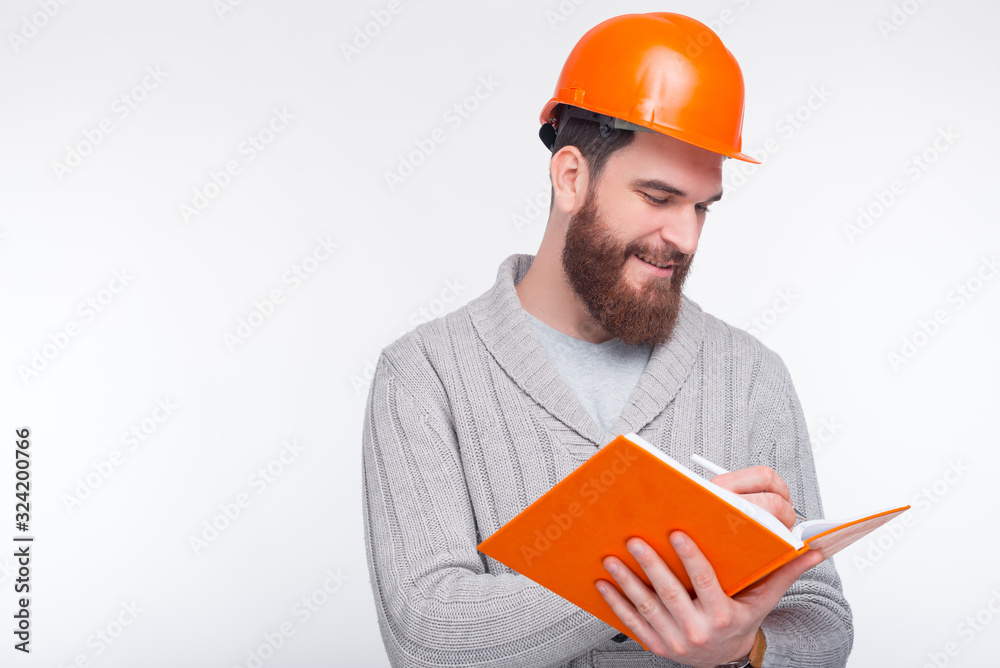 Young smiling engineer wearing hard hat is writing something Young smiling engineer wearing hard hat is writing something