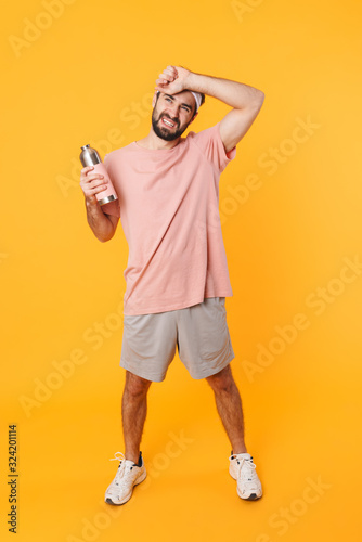 Image of tired athletic young man in t-shirt holding water bottle