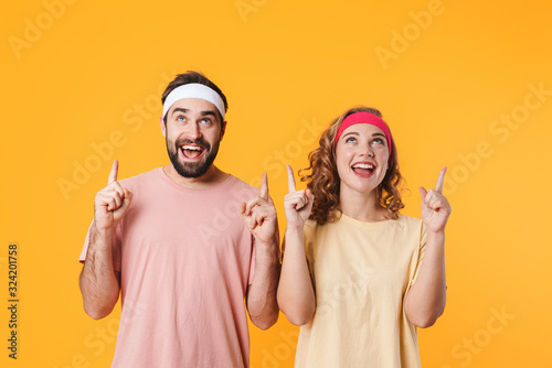Portrait of athletic couple smiling and pointing fingers at copyspace