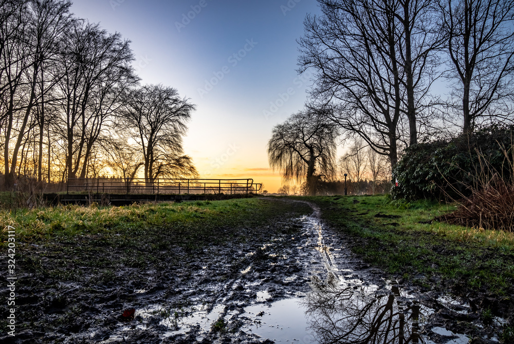A muddy road along a canal during the sunset in the Netherlands A muddy road along a canal during the sunset in the Netherlands