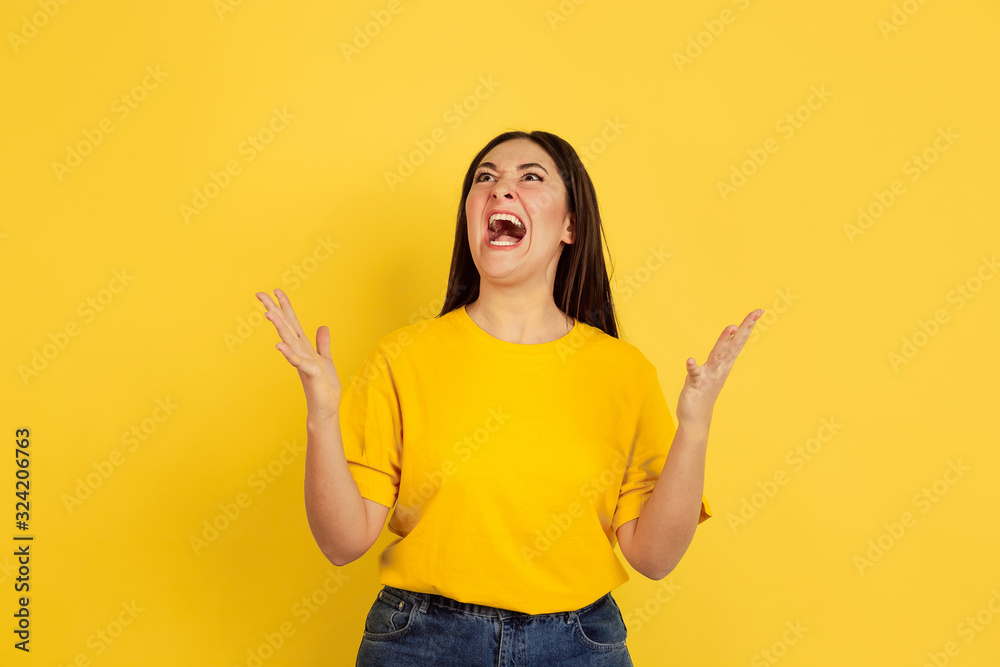 Angry screaming. Caucasian woman's portrait isolated on yellow studio background. Beautiful female brunette model in casual style. Concept of human emotions, facial expression, sales, ad, copyspace. Angry screaming. Caucasian woman's portrait isolated on yellow studio background. Beautiful female brunette model in casual style. Concept of human emotions, facial expression, sales, ad, copyspace.