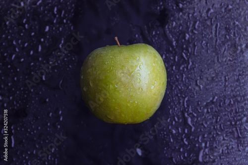 A ripe, juicy green apple hangs on a black background with water drops