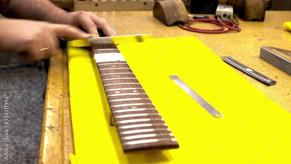 luthier polishing the frets of an electric guitar in his workshop near a window