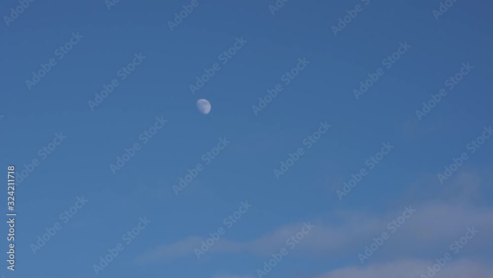 Full moon on partly cloudy blue sky at day Full moon on partly cloudy blue sky at day