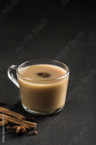 Popular Asian warming drink masala tea in a clear glass cup with coriander, cinnamon and rose stem on a black background.