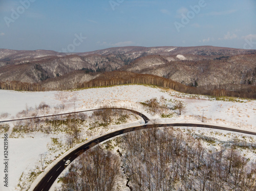 Early winter on the slopes of Ashikawa, Hokkaido Japan where the trees have shed their leaves and there is a layer of snow on the ground with the junction between two mountain roads as the foreground 