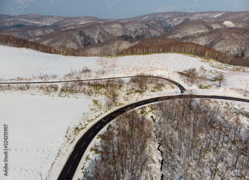 Early winter on the slopes of Ashikawa, Hokkaido Japan where the trees have shed their leaves and there is a layer of snow on the ground with the junction between two mountain roads as the foreground  photo