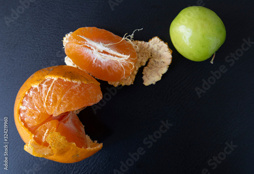 Top view, orange peeled by hand, placing on floor with green jujube. Healthy fresh orange. Healthy diet concept. Peeled oranges placed on black floor. Concept differenc in same place photo