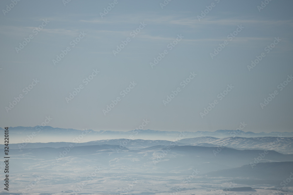 Beautiful view of the mountain range partially covered by fog and snow with clear blue sky.