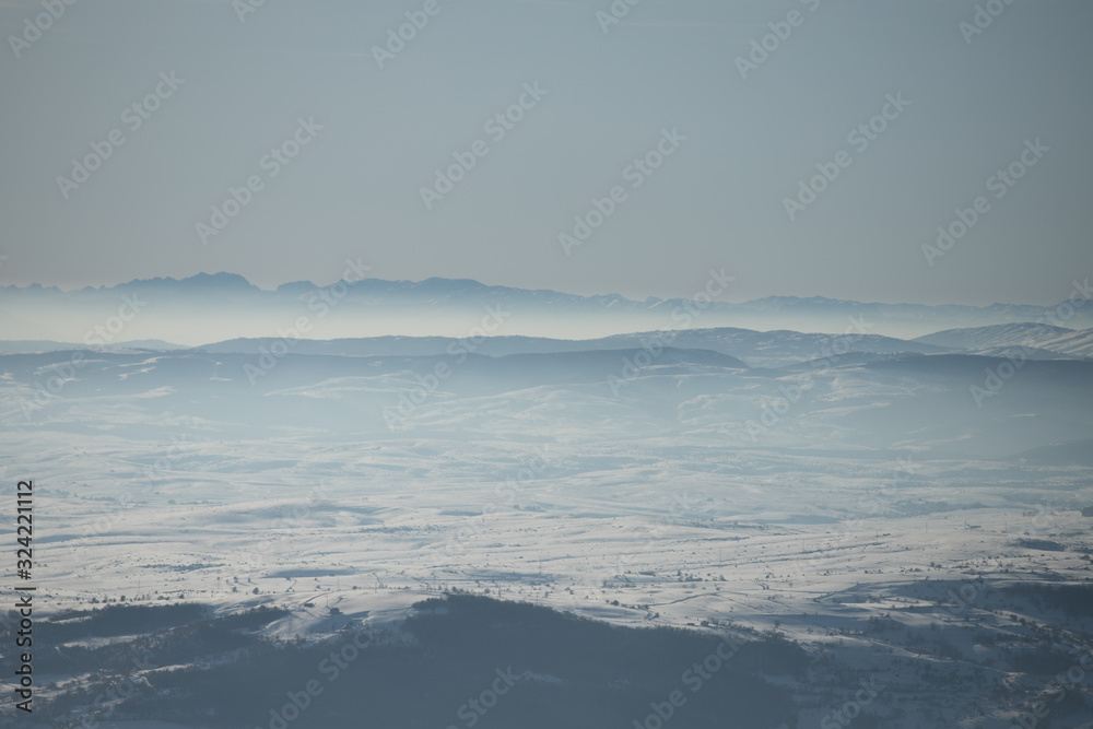 Beautiful view of the mountain range partially covered by fog and snow with clear blue sky.